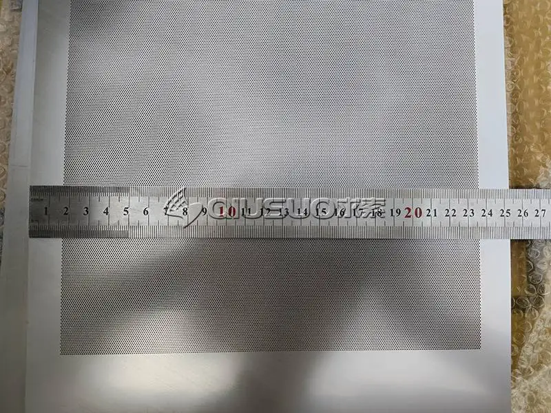 A worker is measuring the width of the etched metal mesh.